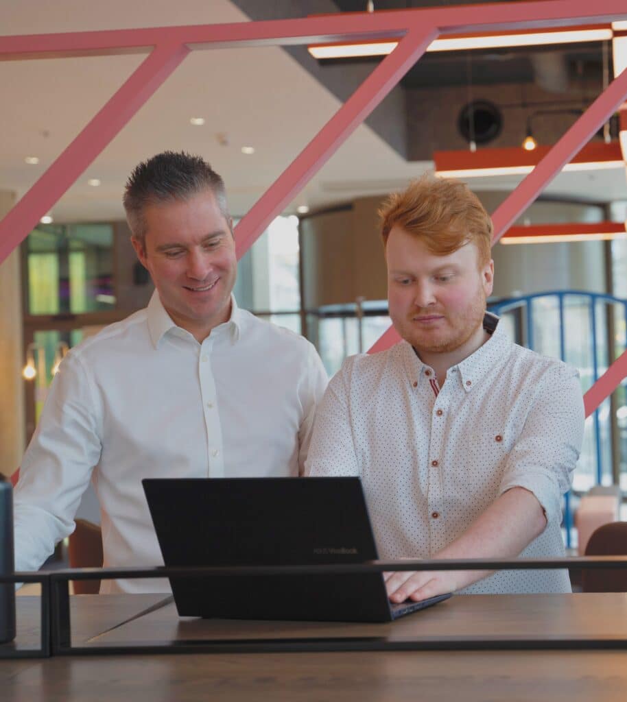 Two Equilibrium team members collaborating at a laptop in a modern office setting.